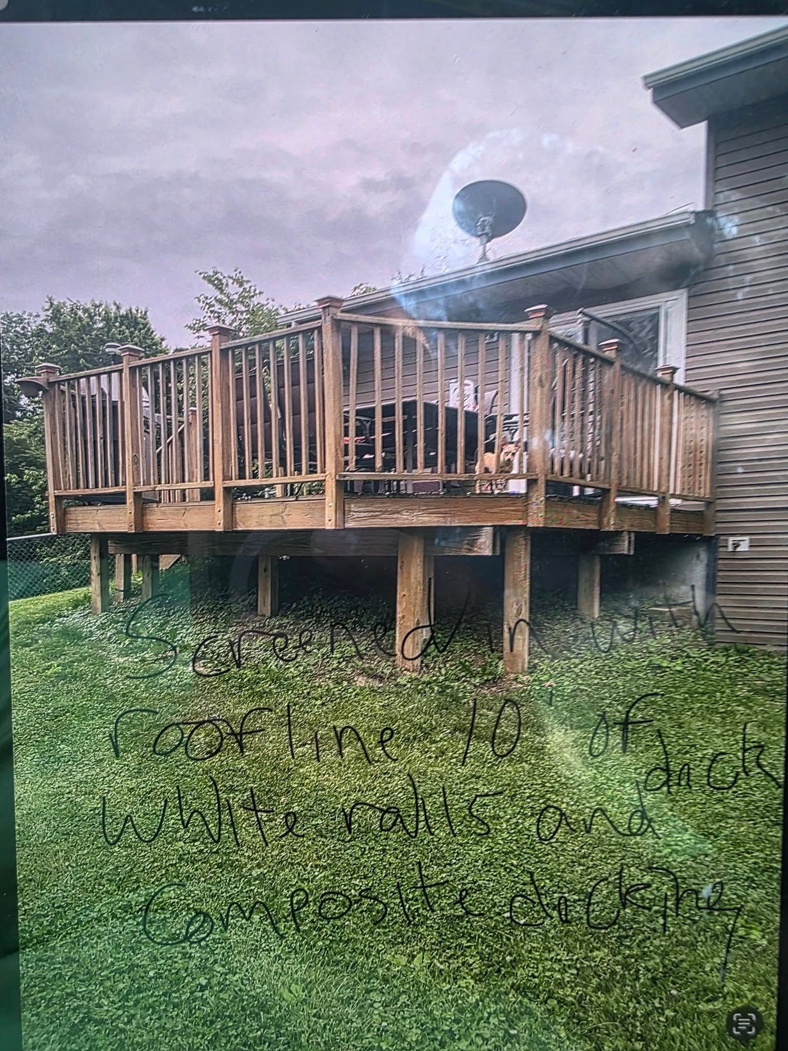 A wooden deck attached to a brick house stands above a sloped, grassy lawn.