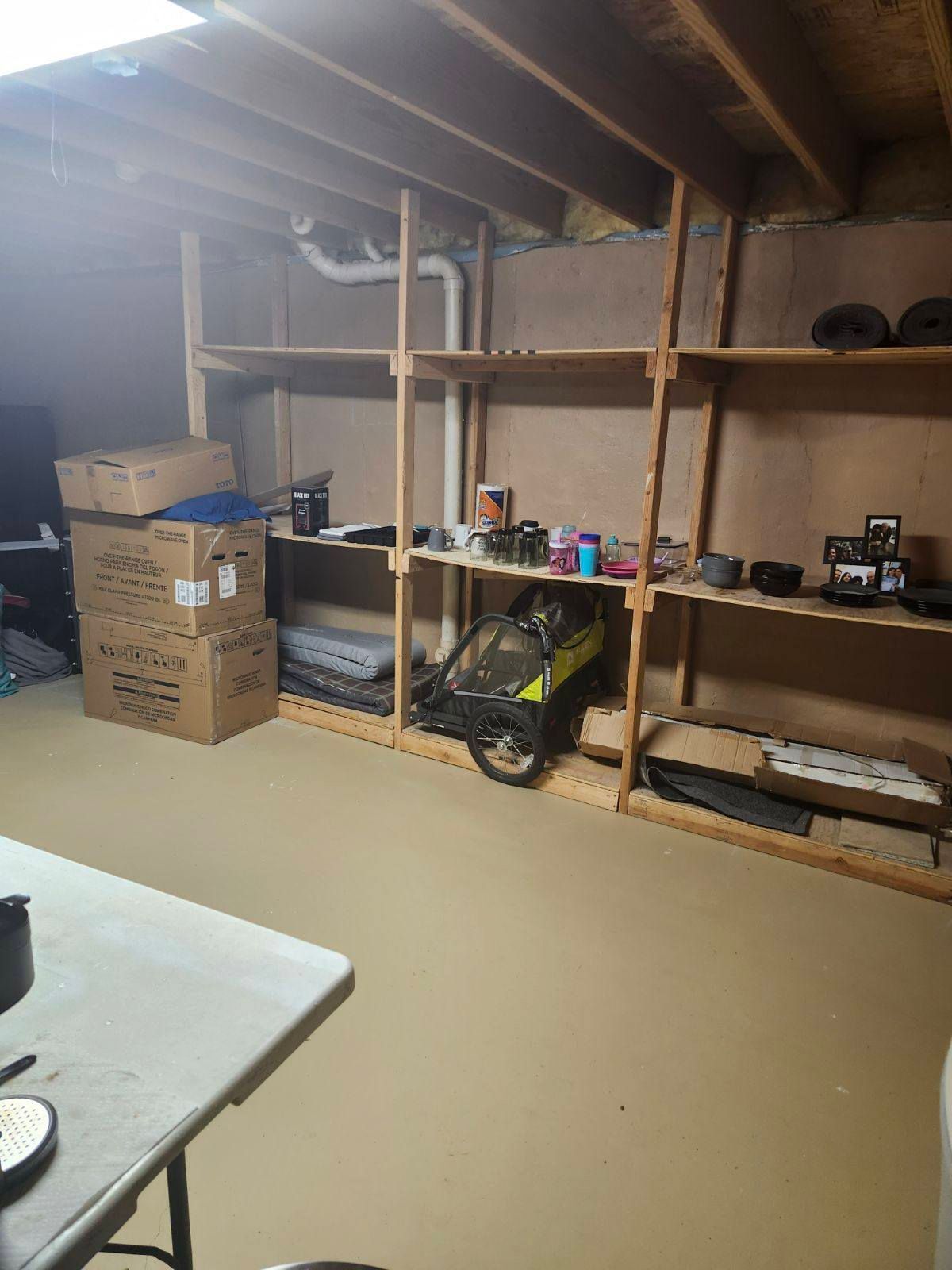 A storage area with wooden shelves holding cardboard boxes, a child's bike trailer, and various items in a basement.