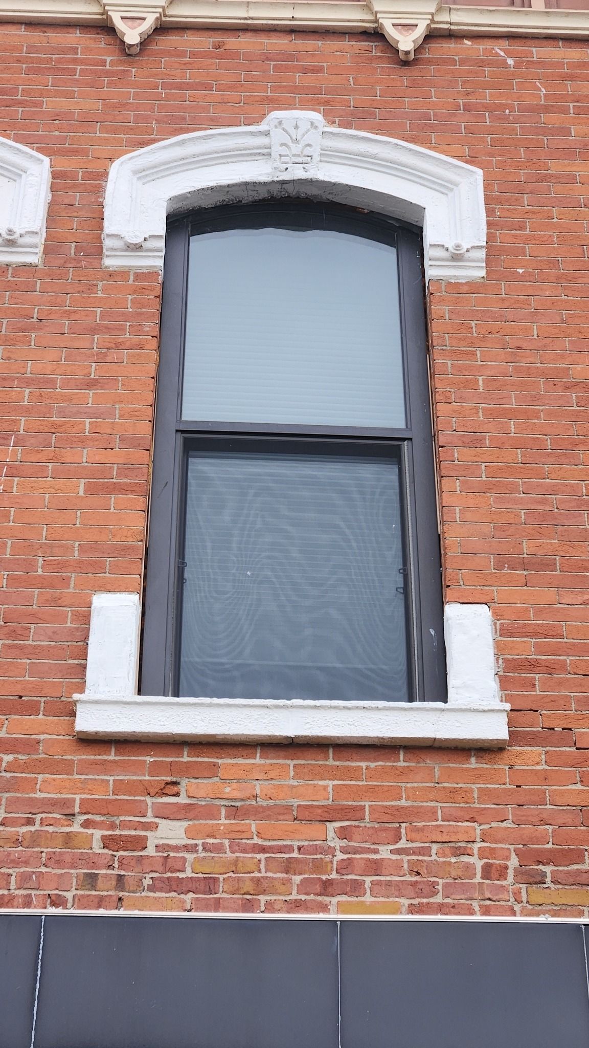 An arched, dark-framed window with a screen and white decorative trim, set into a red brick exterior wall.
