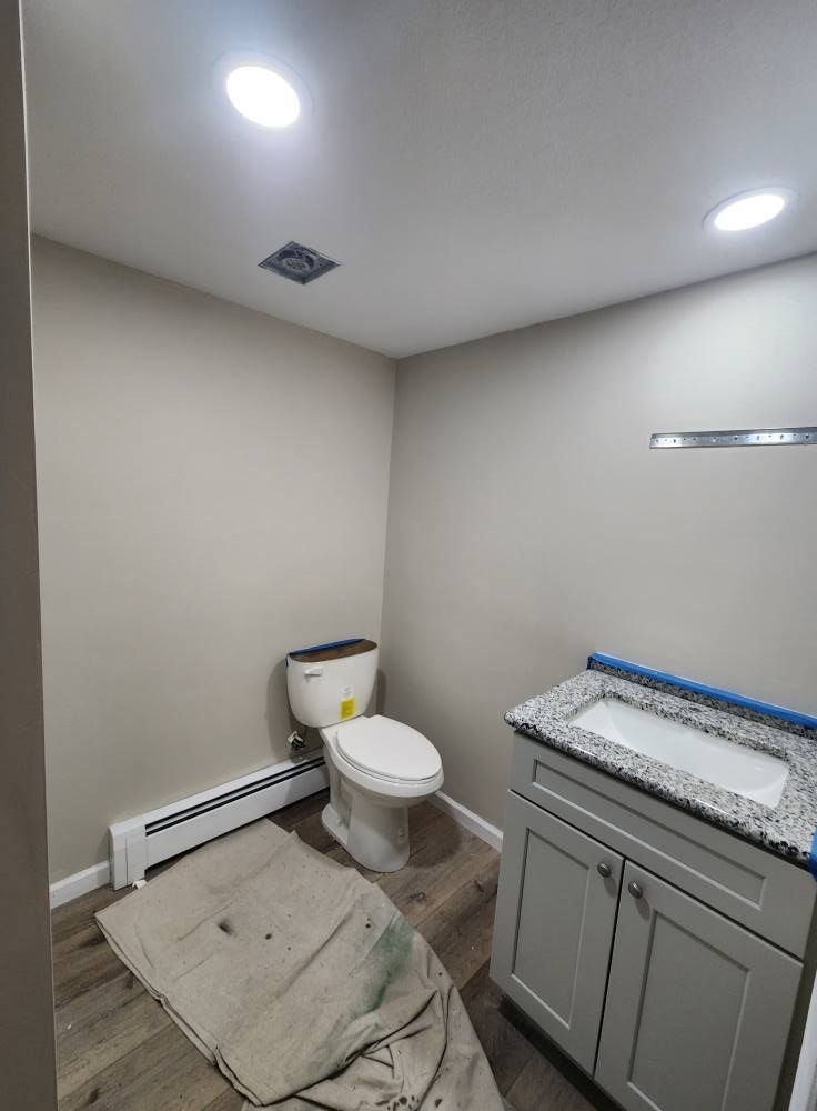 A small, neutrally colored bathroom with a white toilet, gray vanity with a granite countertop, and wood-look flooring.