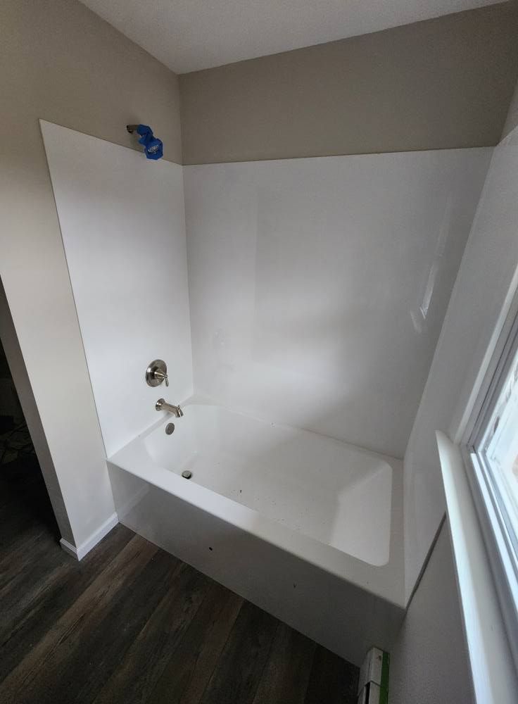 A modern bathroom featuring a white bathtub and shower surround with chrome fixtures, set against light gray walls.