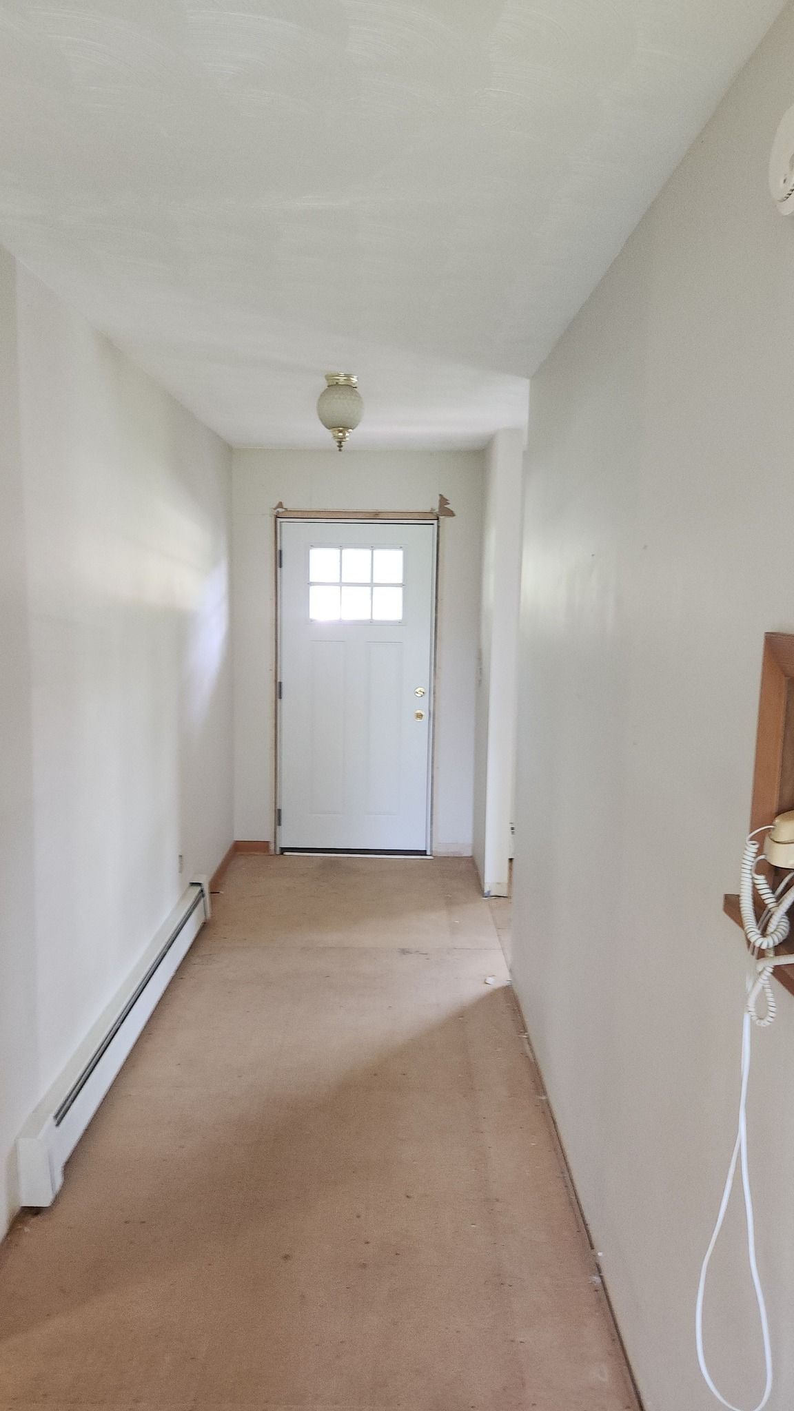 A carpeted hallway with plain white walls leading to a white, six-paneled exterior door with a window.