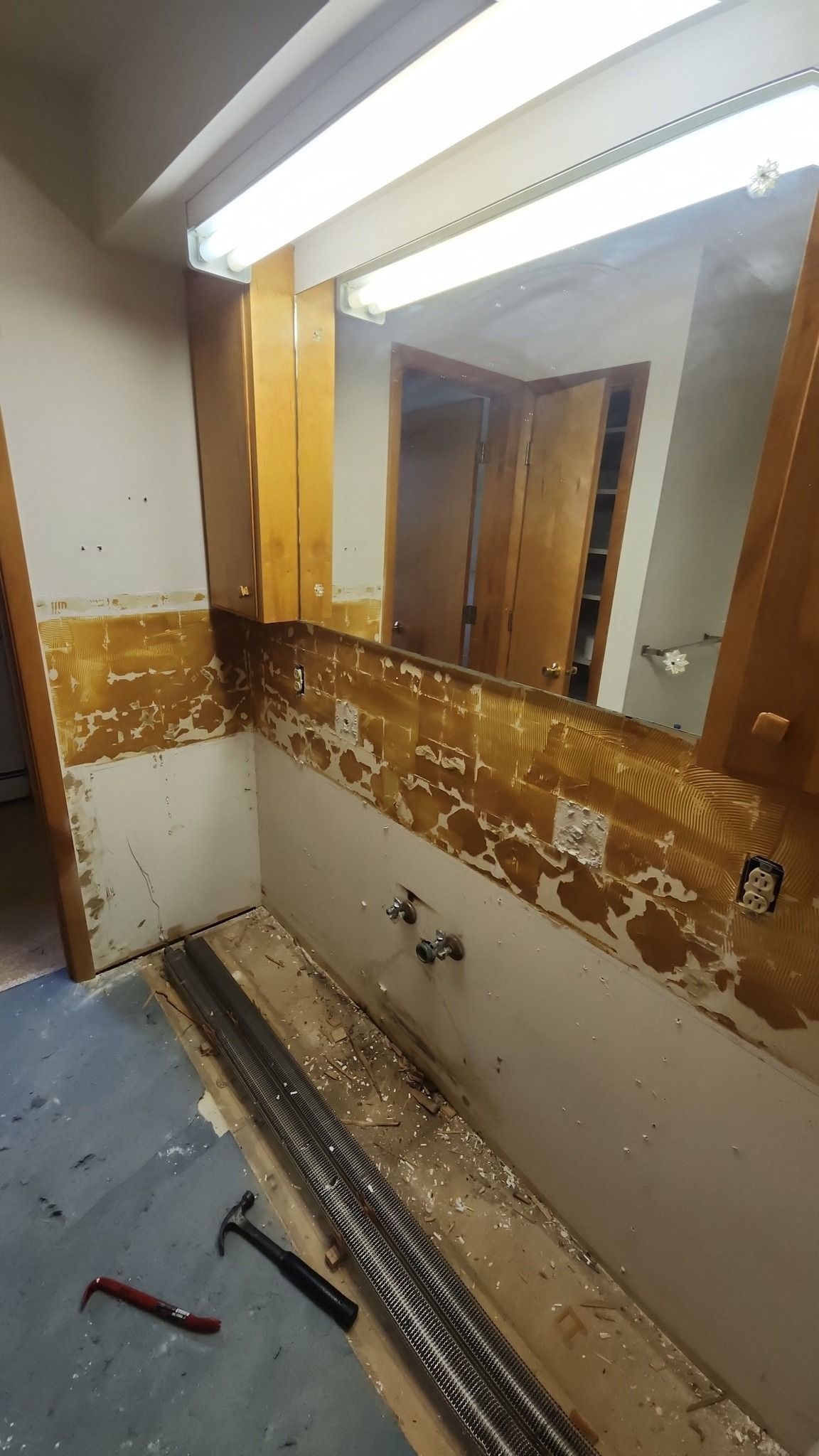 Bathroom renovation in progress with removed vanity, damaged walls, and construction tools on the floor.