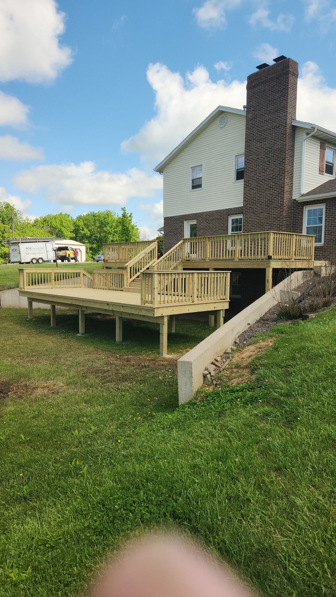 A newly constructed, multi-level wooden deck attached to the rear of a white-sided house with a large brick chimney.