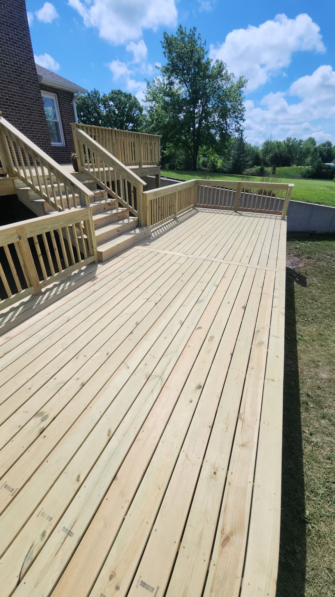 A newly built wooden deck with stairs leading up to a brick house under a blue, cloudy sky.