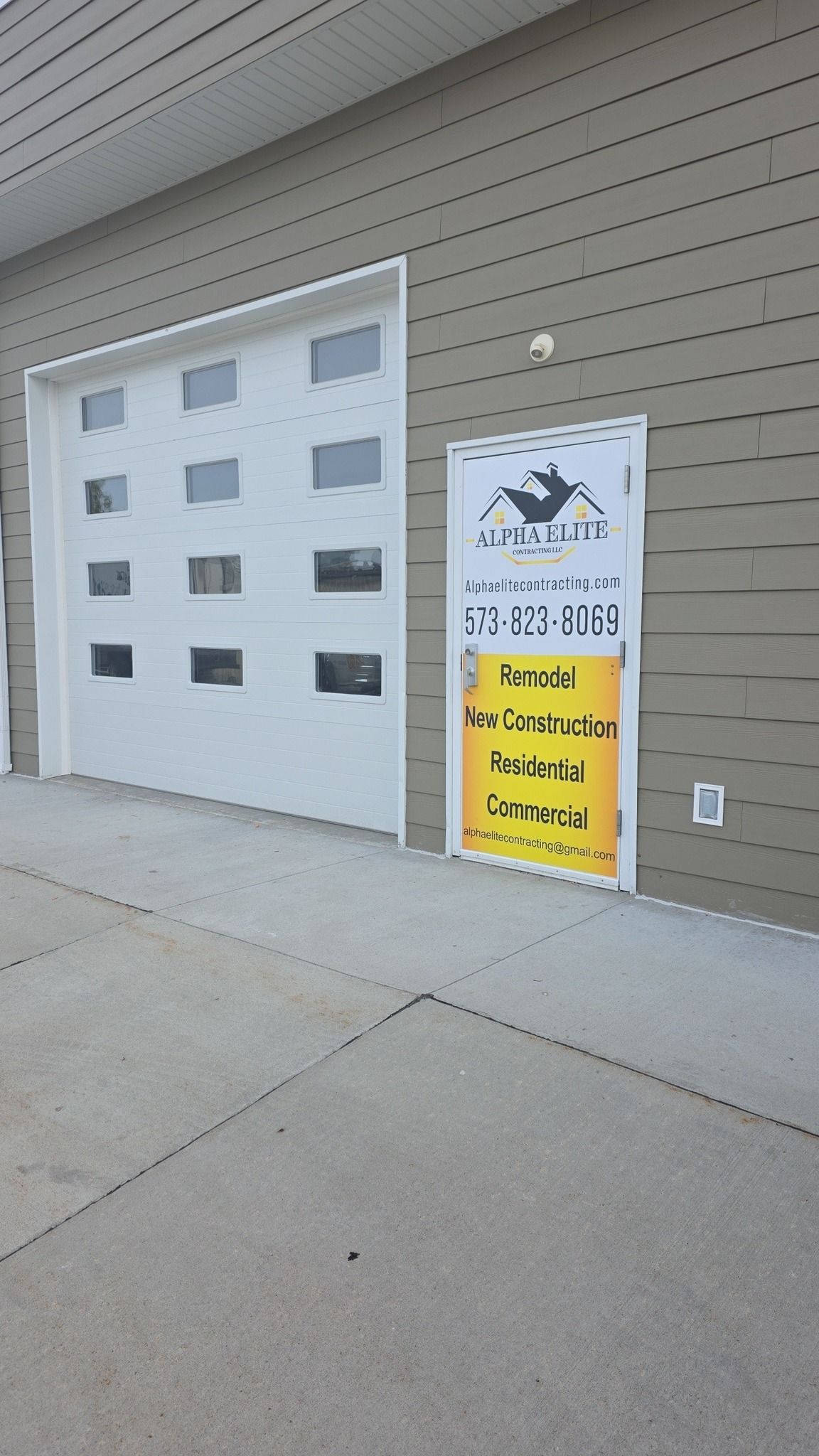 A tan building exterior featuring a white garage door and an informational sign with text and a crow logo next to it.