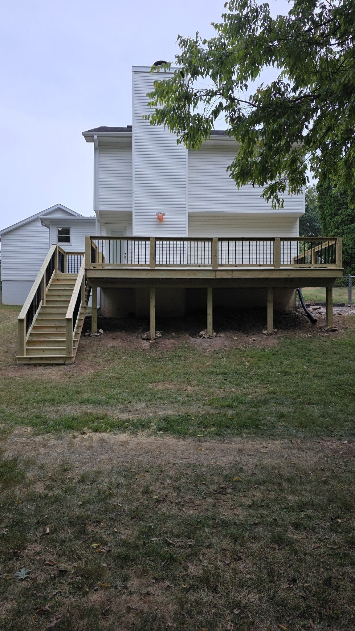A new wooden deck with a staircase attached to the back of a white two-story house with a prominent chimney.