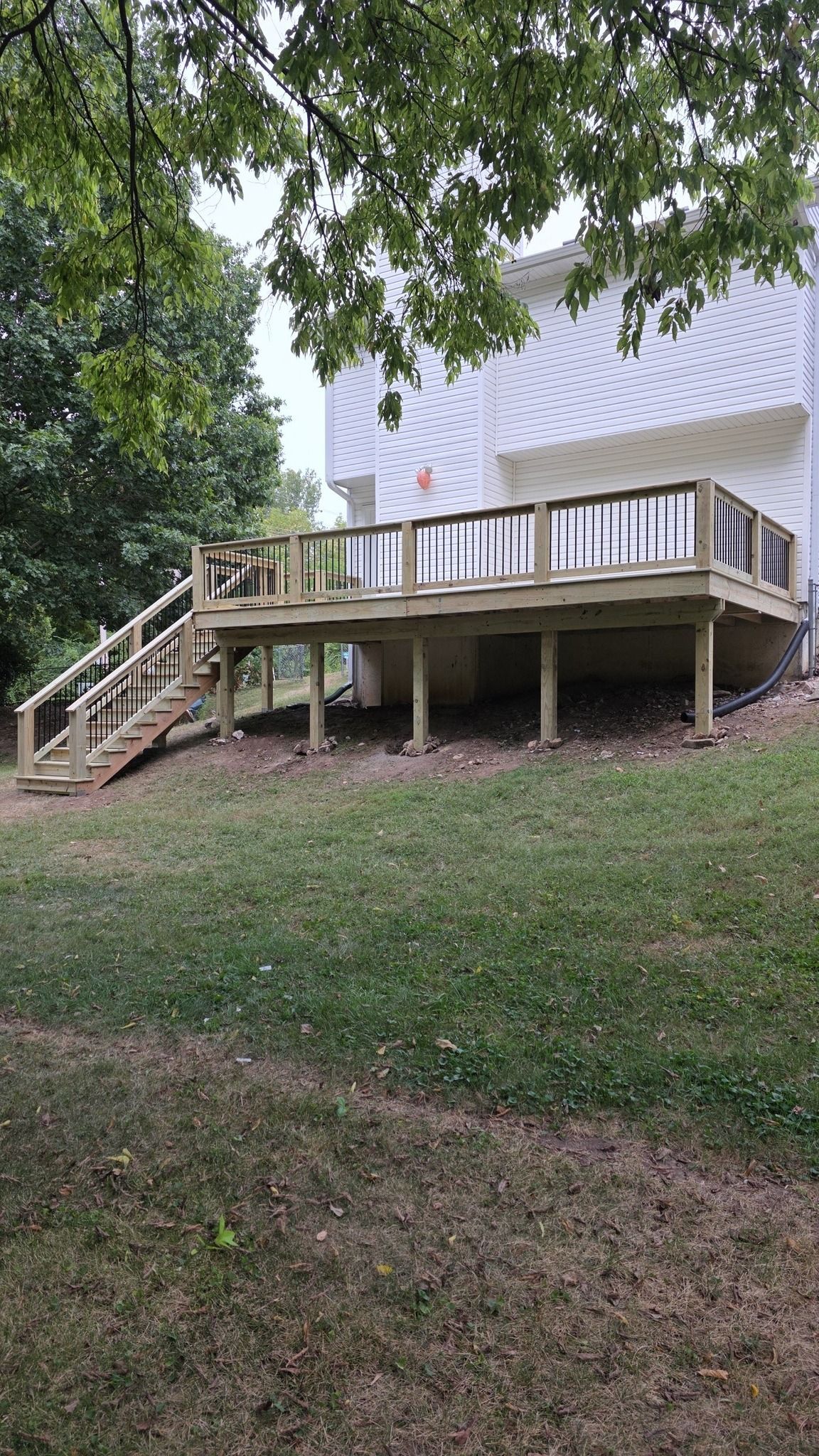 A wooden deck with railings and stairs attached to the back of a white house on a grassy hill.
