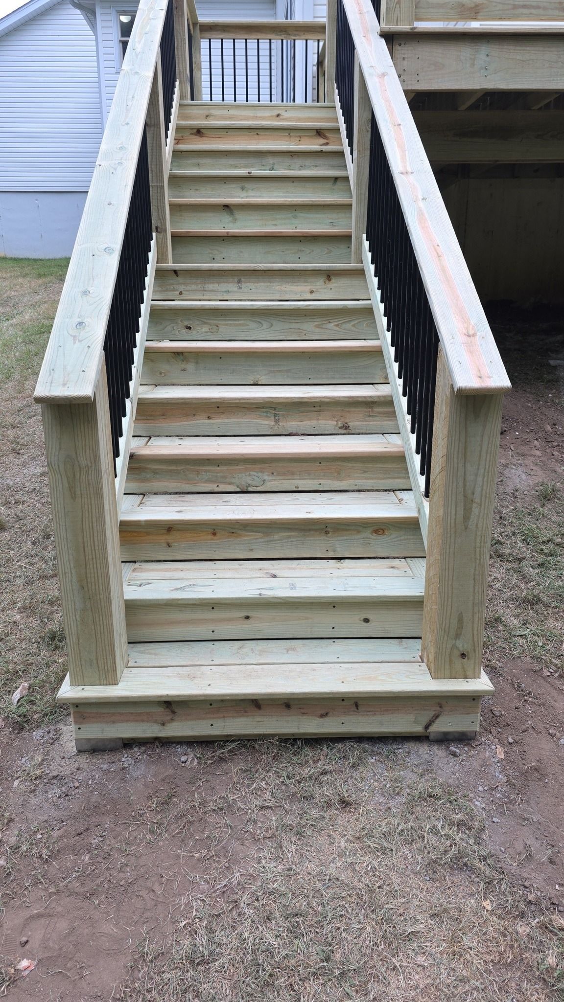 Newly constructed wooden outdoor staircase with railings, leading to a raised deck in a backyard.