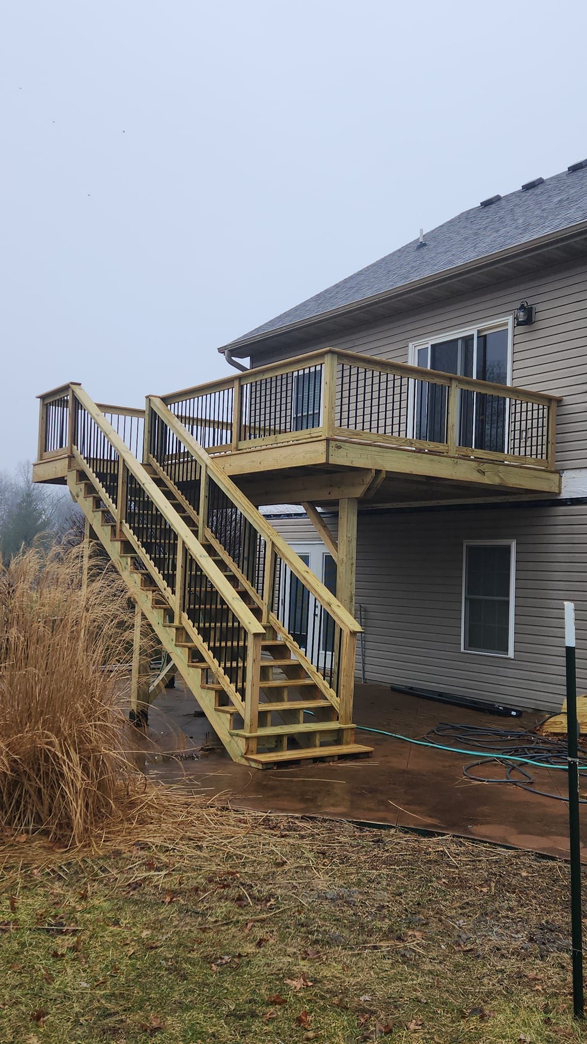 A newly constructed wooden deck and staircase attached to the back of a house over a concrete patio.