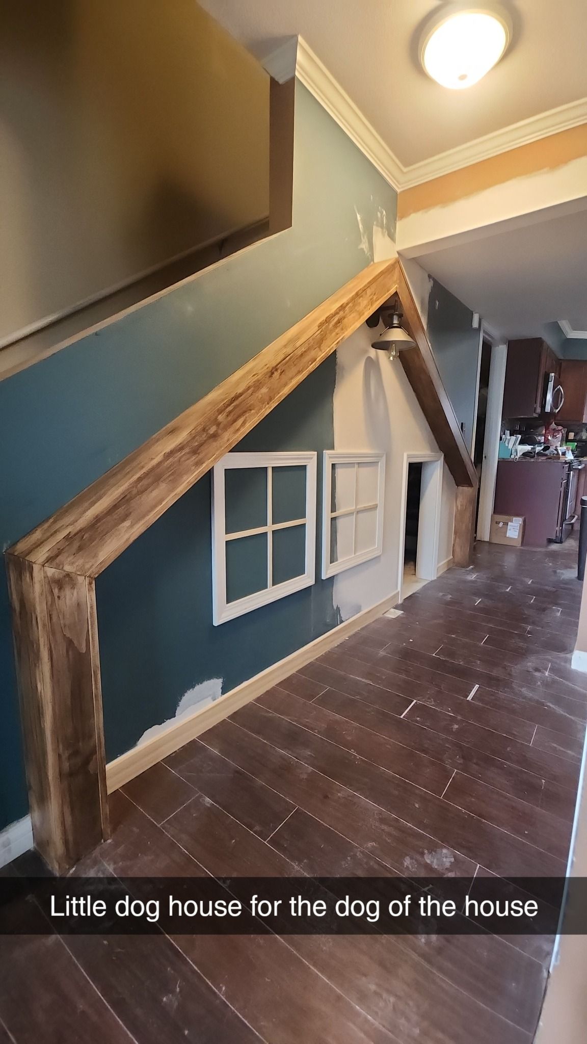 A custom dog house built into the space under a staircase, featuring a wooden frame, white windows, and painted walls.