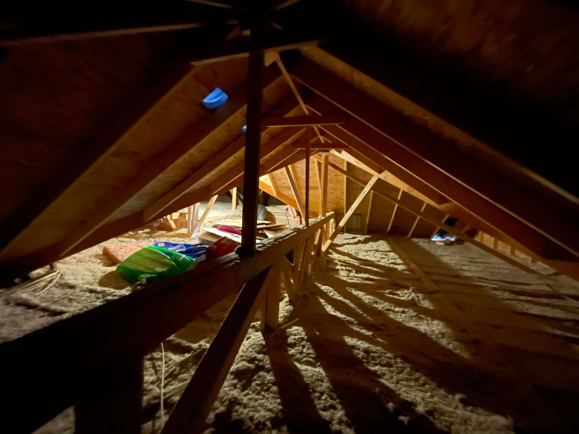 Attic interior featuring wooden roof rafters, insulation covering the floor, and a wooden support beam structure.