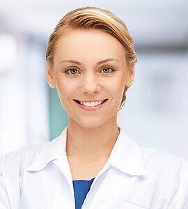Woman in white coat smiles, blurry background, likely in medical setting.