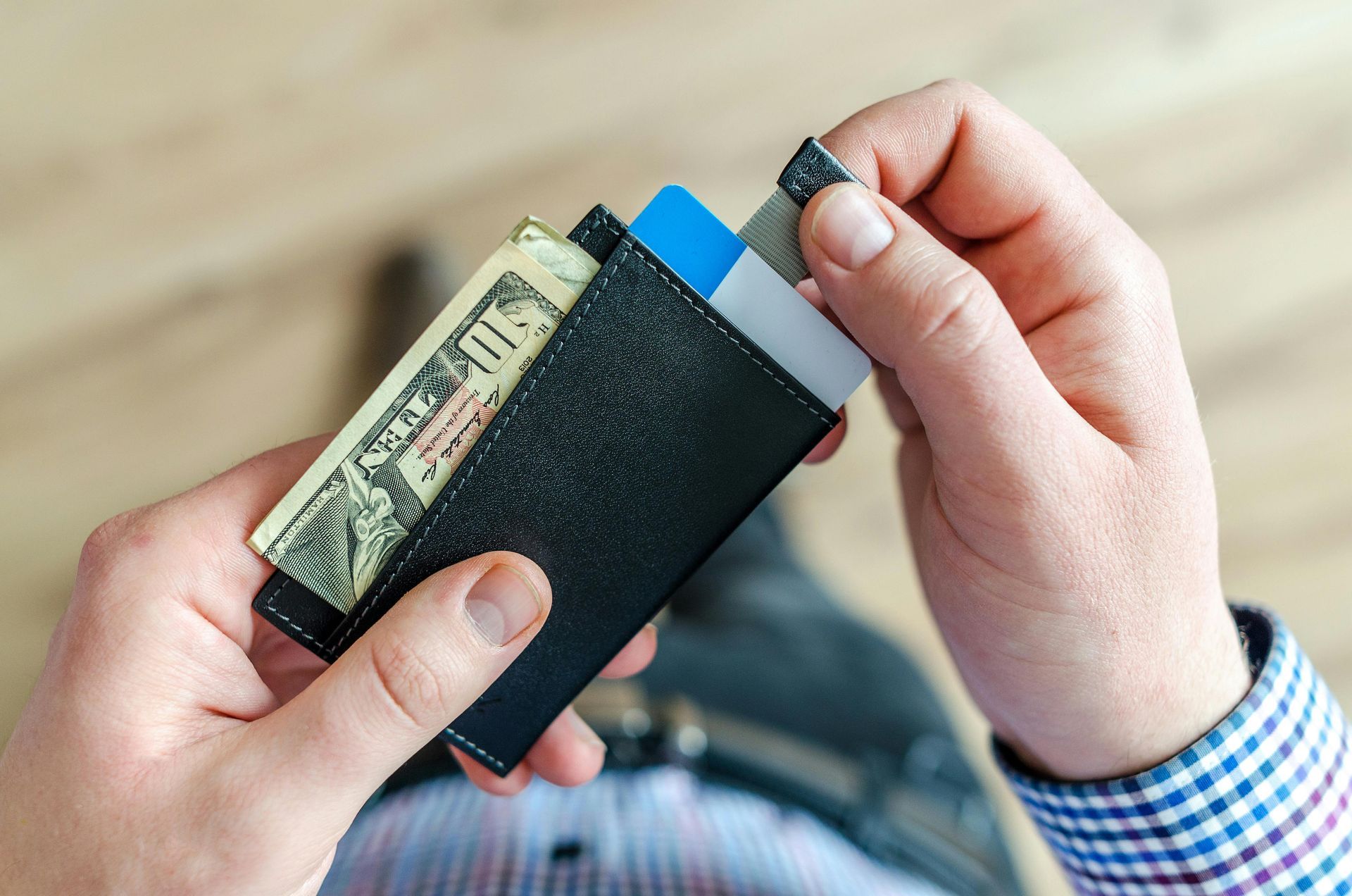 Person holding a black wallet with money and cards, indoors, close-up.