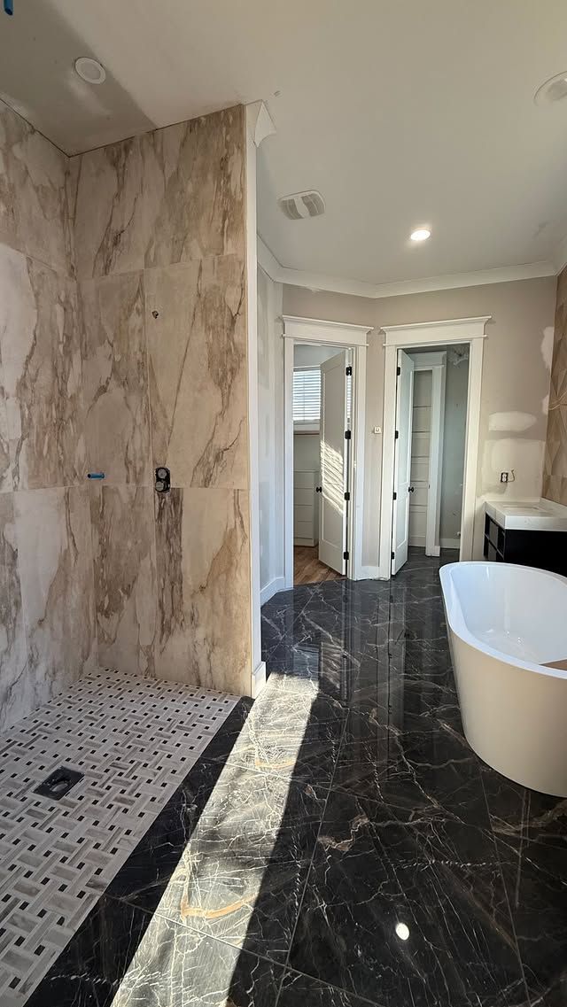 Luxurious bathroom with marble shower and black marble floor. White tub and doors.