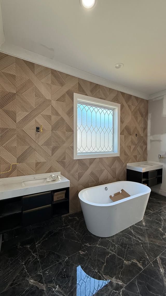 Bathroom with wood-look tile wall, white tub, dark vanity, and marble-like floor. A window is visible.
