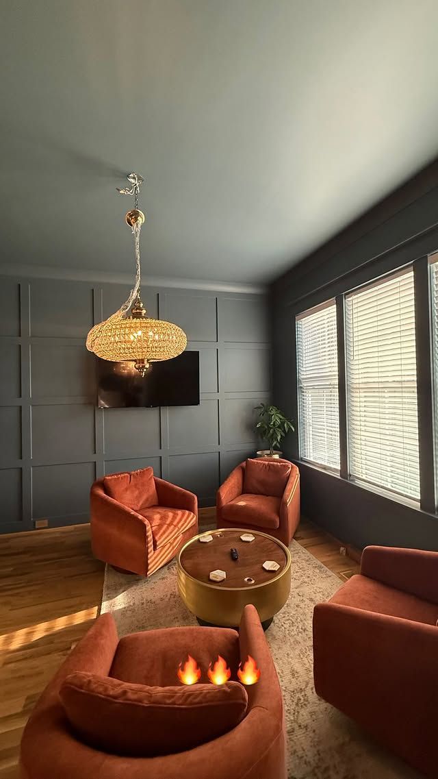 Living room with orange armchairs, gold ottoman, and ornate chandelier, on a rug.