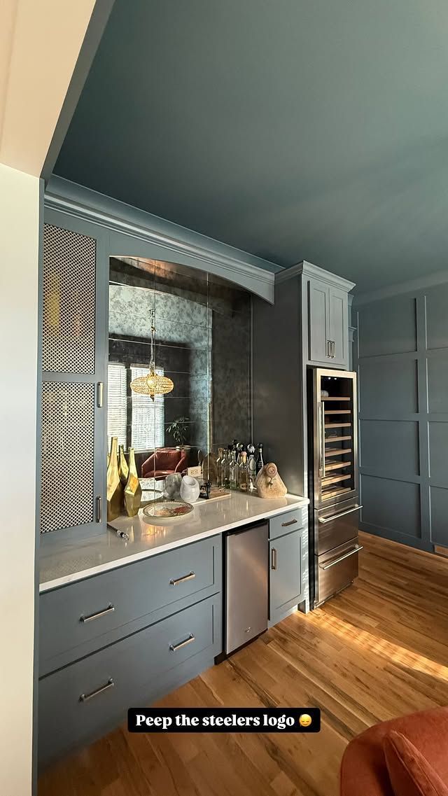 A built-in home bar with gray cabinets, a mirrored backsplash, and a wine fridge.