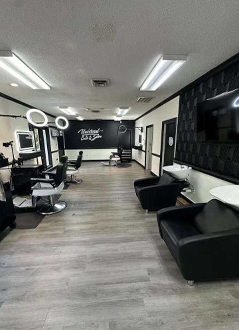 Hair salon interior with black chairs, mirrors, and light-colored wood-look floor. White walls, black accent wall.
