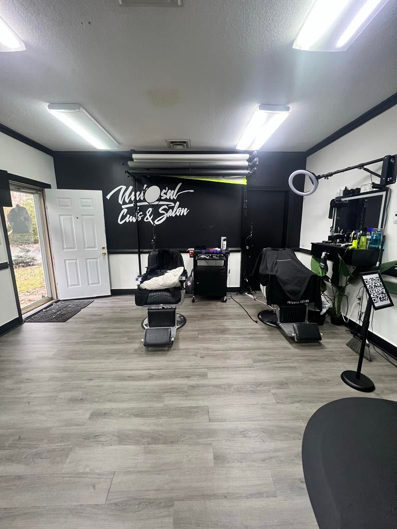 A barbershop interior with chairs, equipment, and a neon sign on a black wall.