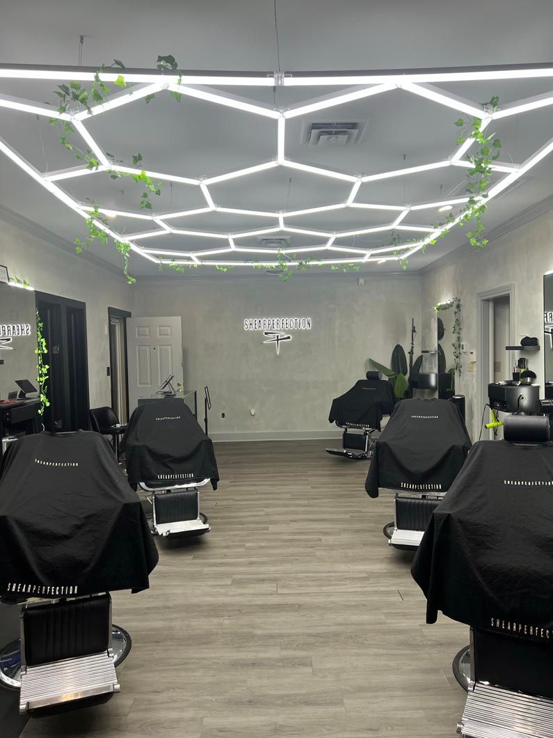 Barber shop interior with hexagonal lights, chairs covered in black capes, and a logo on the wall.