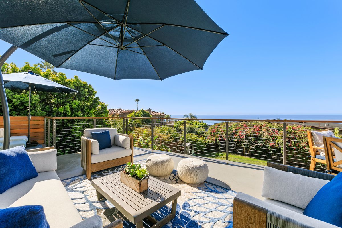 A patio with furniture and umbrellas overlooking the ocean.
