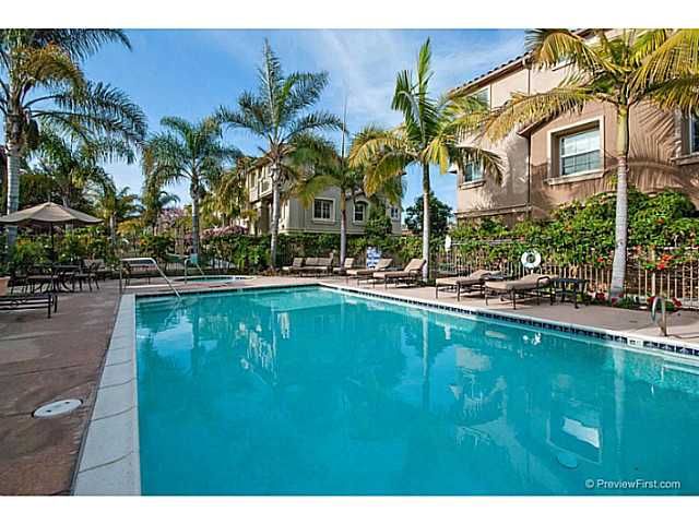 A large swimming pool surrounded by palm trees and chairs in front of a building.