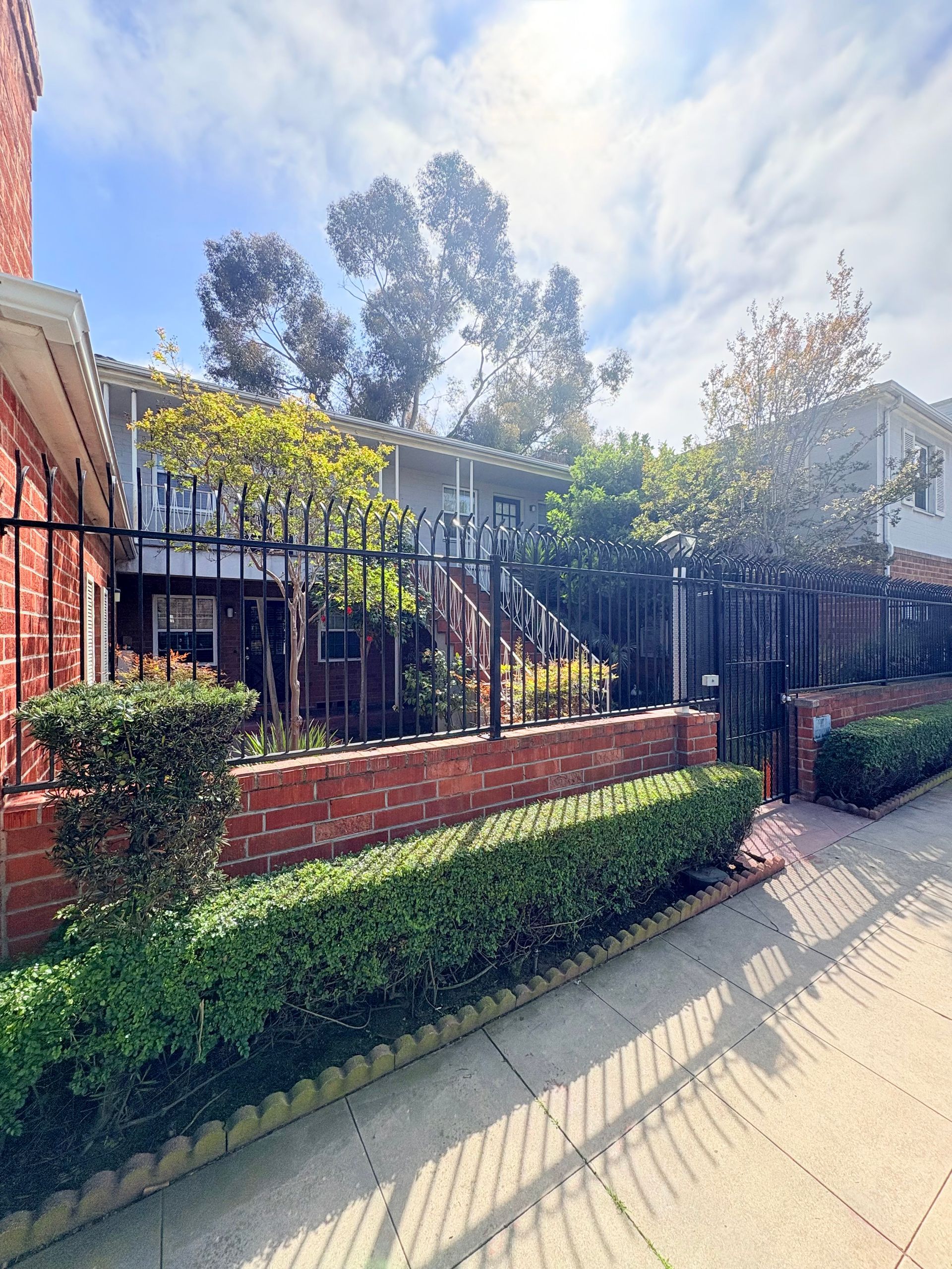 A brick building with a fence and bushes in front of it.