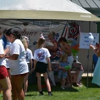 A group of people are standing under a tent in the grass.