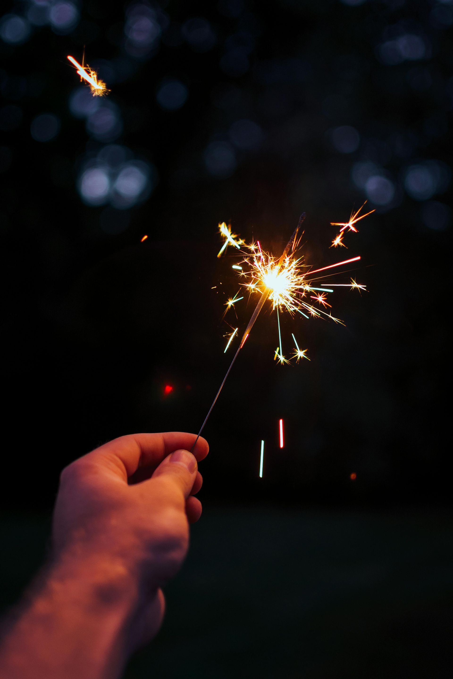 A person is holding a sparkler in their hand in the dark.