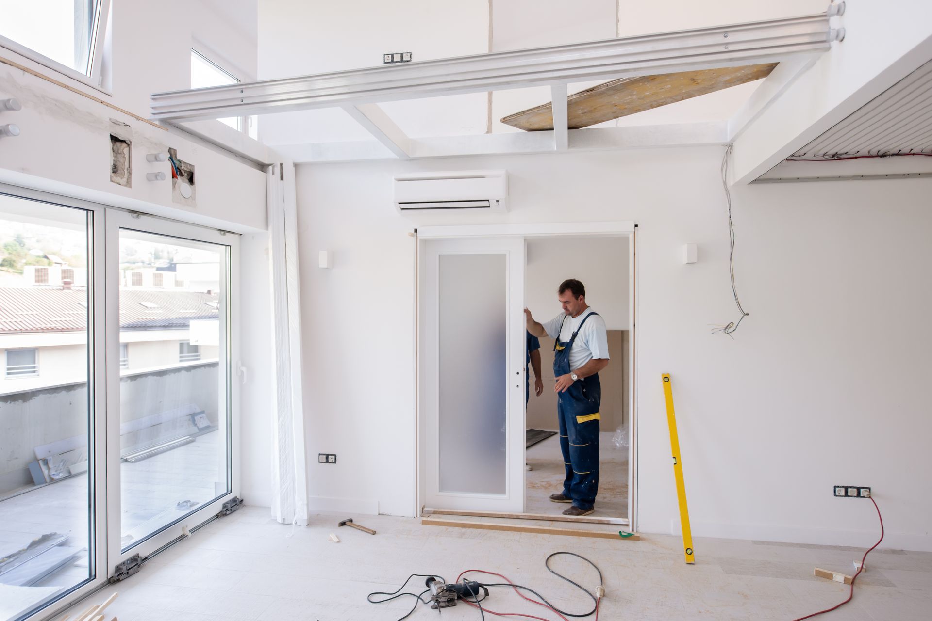 Door Installation — Man in overalls installing a sliding door in a bright, newly renovated room in Cranberry Township, PA