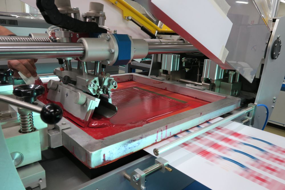 A Screen-printing Machine Applying Red Ink Onto Fabric With a Plaid Pattern — C & D Manufacturing In Caboolture, QLD