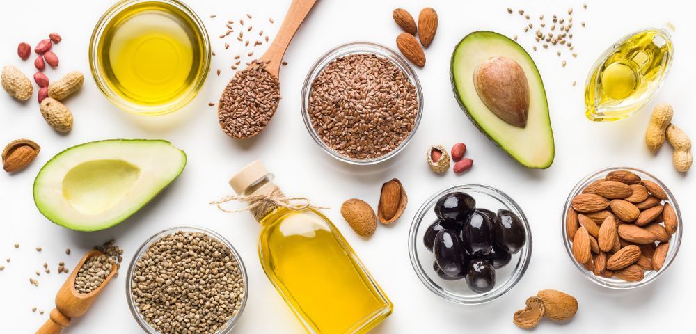 Assortment of Healthy Fats: Oils, Avocados, Seeds, Nuts, and Olives on a White Surface — C & D Manufacturing In Caboolture, QLD