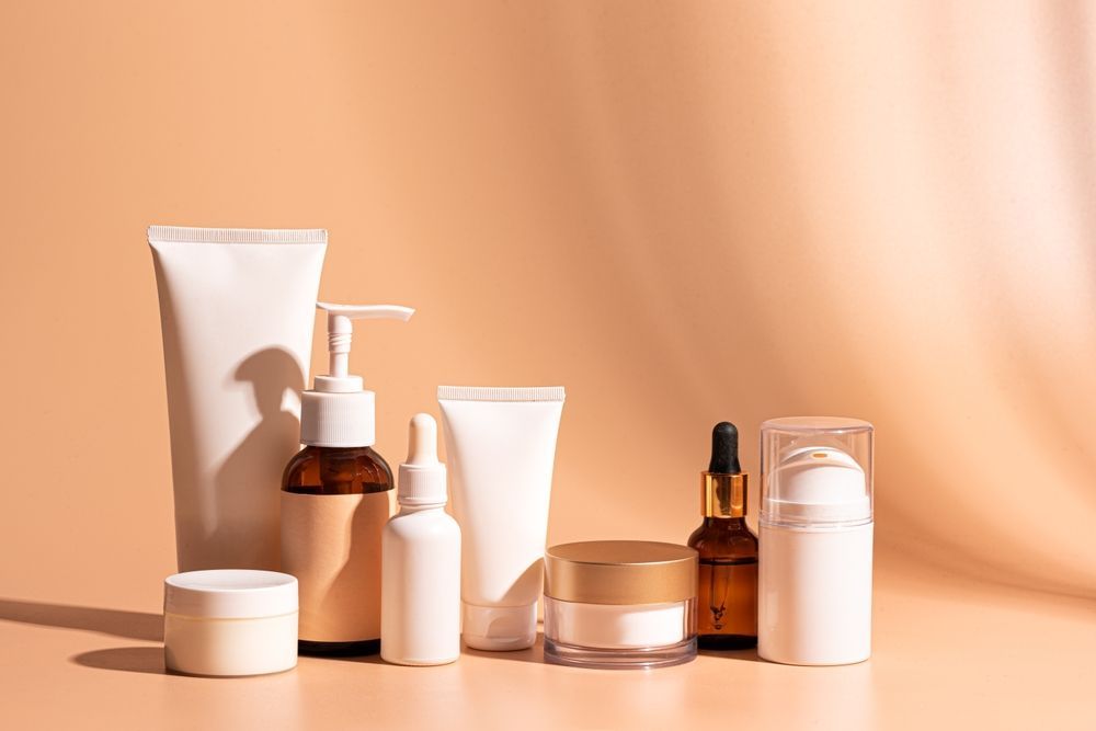 Cosmetic Products in Various Containers, Mostly White and Tan, Arranged on a Peachy Background With Shadows — C & D Manufacturing In Caboolture, QLD