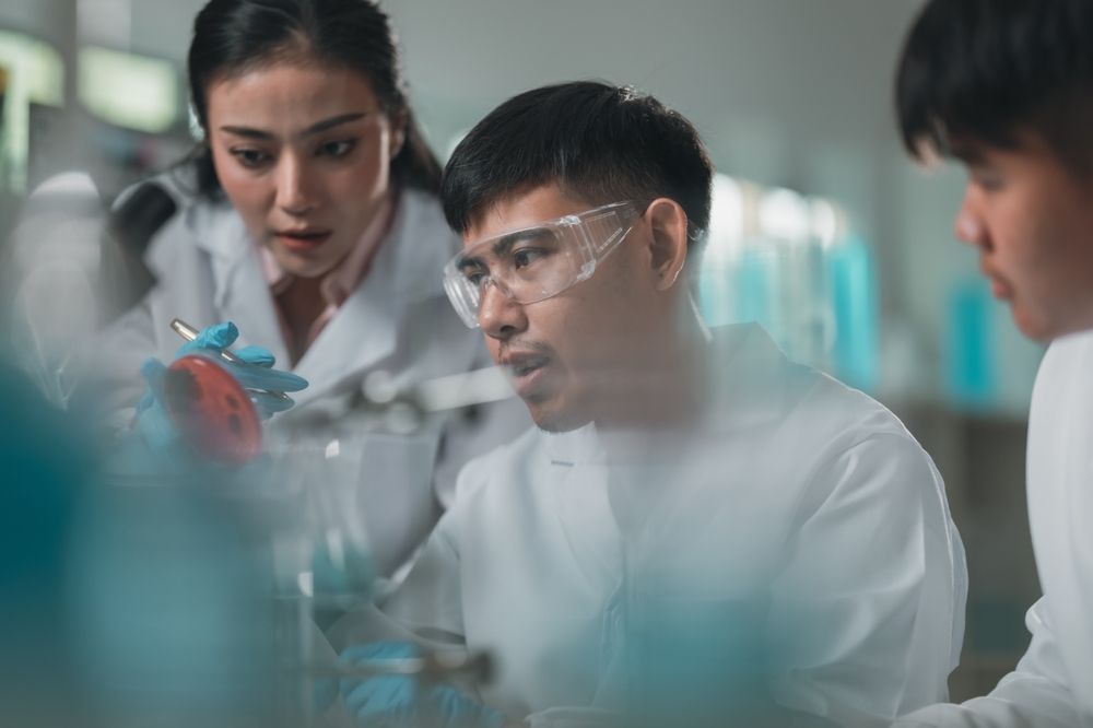 Three Scientists in Lab Coats and Safety Glasses Examining a Container With a Red Substance, Possibly in a Lab Setting — C & D Manufacturing In Caboolture, QLD