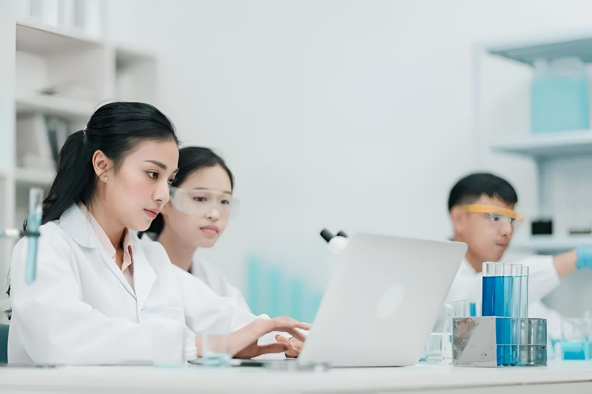 Three Scientists in Lab Coats Working in a Laboratory. One Woman Types on a Laptop, While the Others Are Focused on Lab Equipment — C & D Manufacturing In Caboolture, QLD