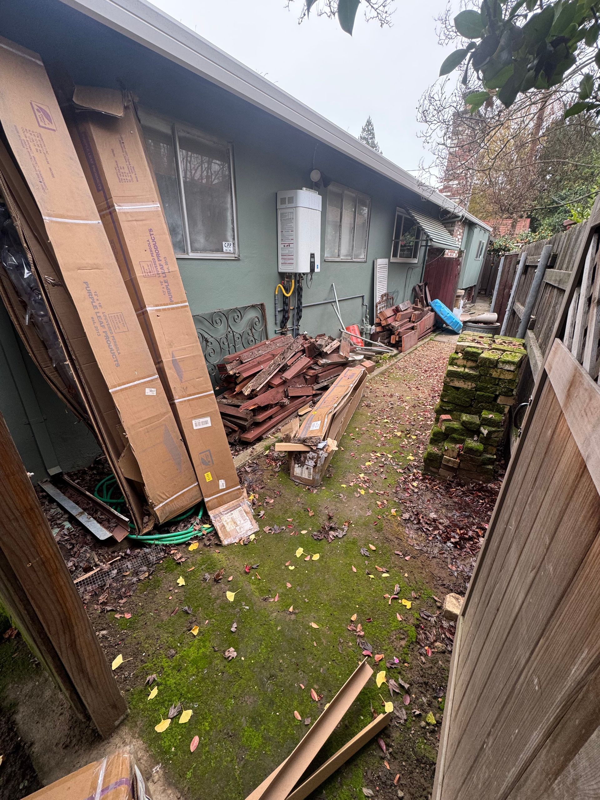 Backyard with building, debris, and cardboard. Green grass and moss, cloudy sky.