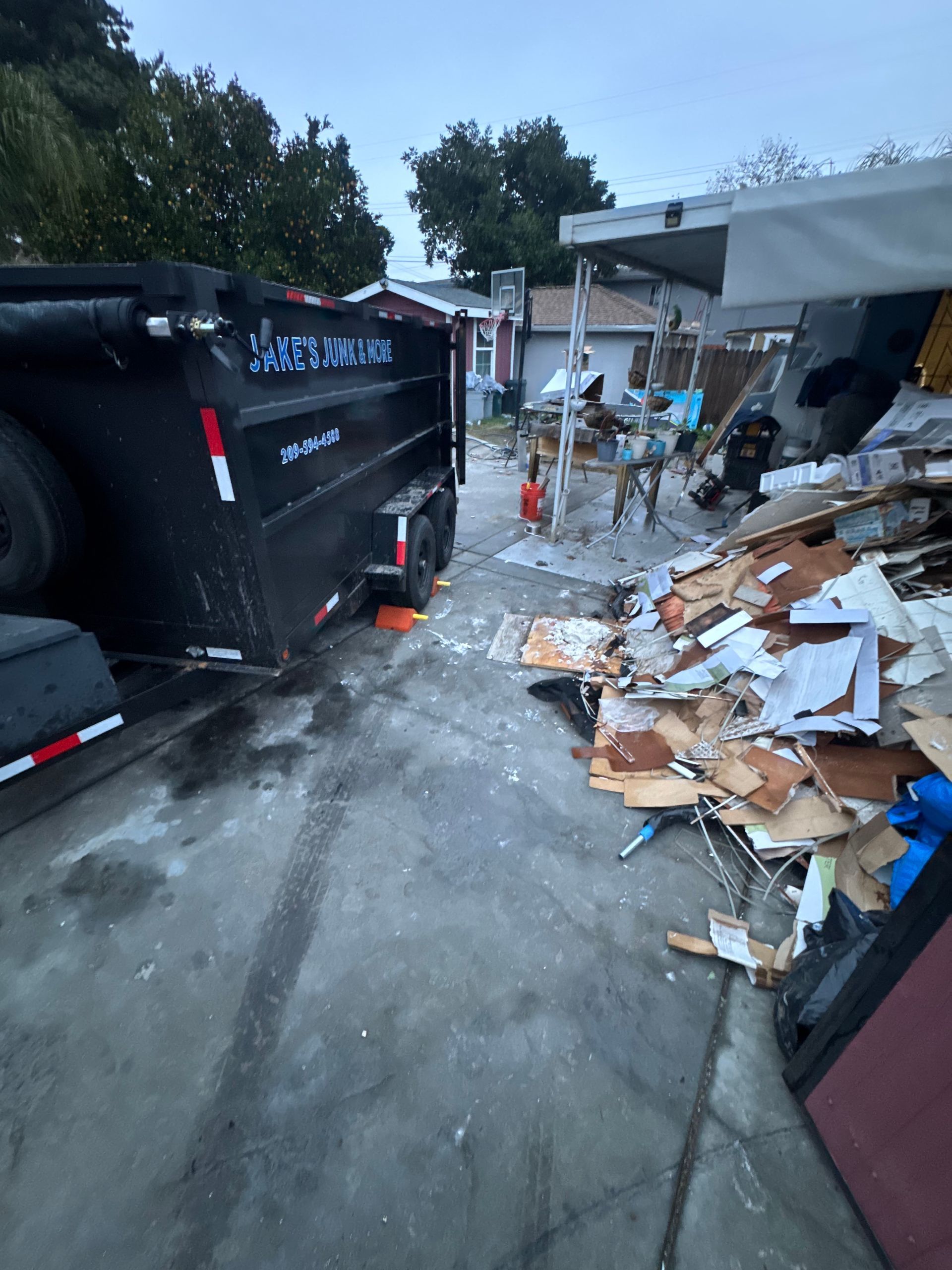 A black dumpster trailer next to a pile of construction debris outdoors.