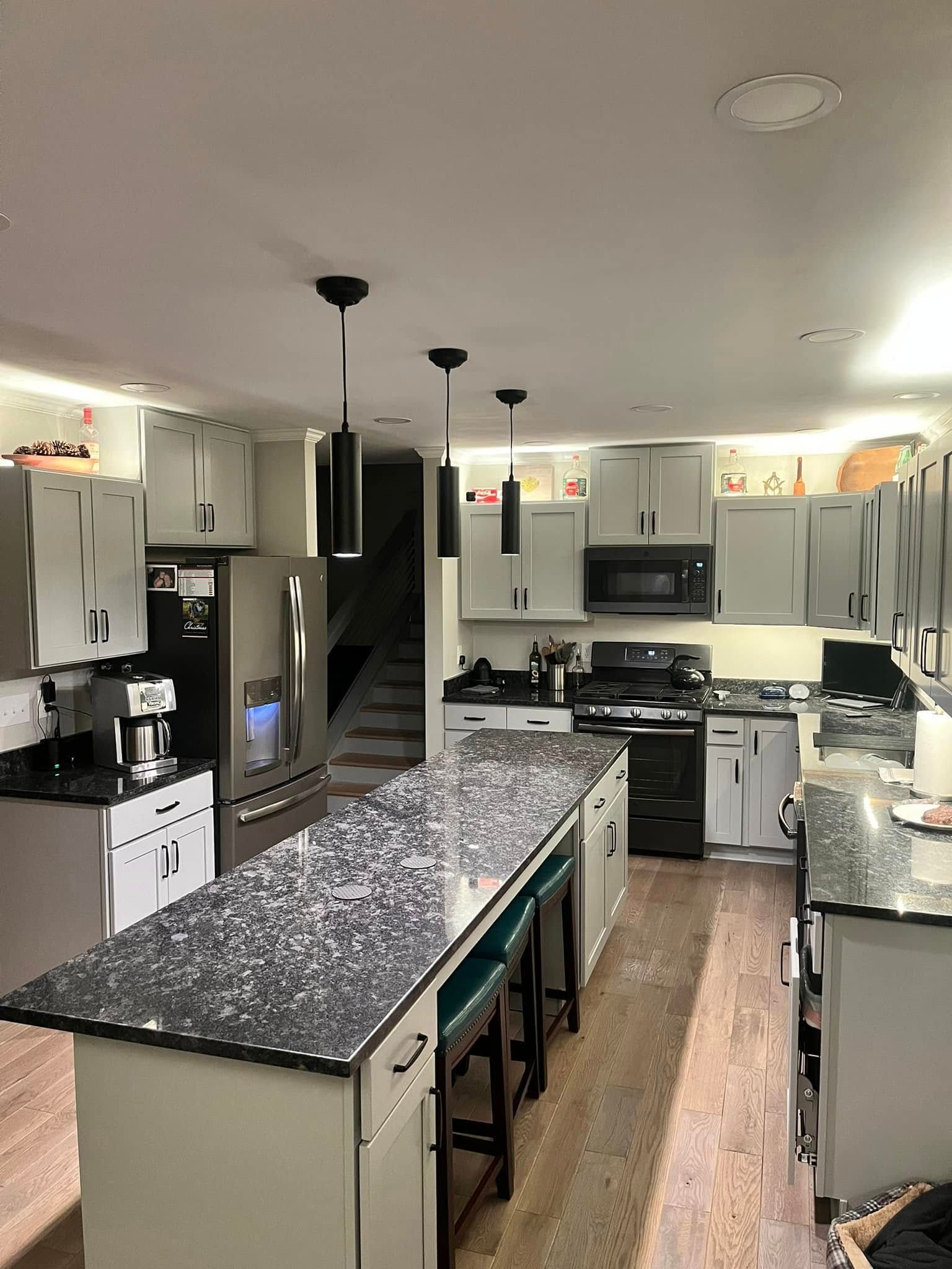 Kitchen with light gray cabinets, black countertops, island with stools, and stainless steel appliances.
