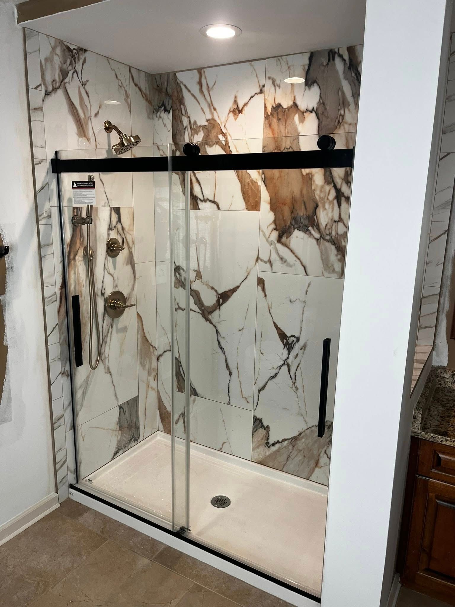 Modern shower with marble-look tile, sliding glass door, and black hardware.