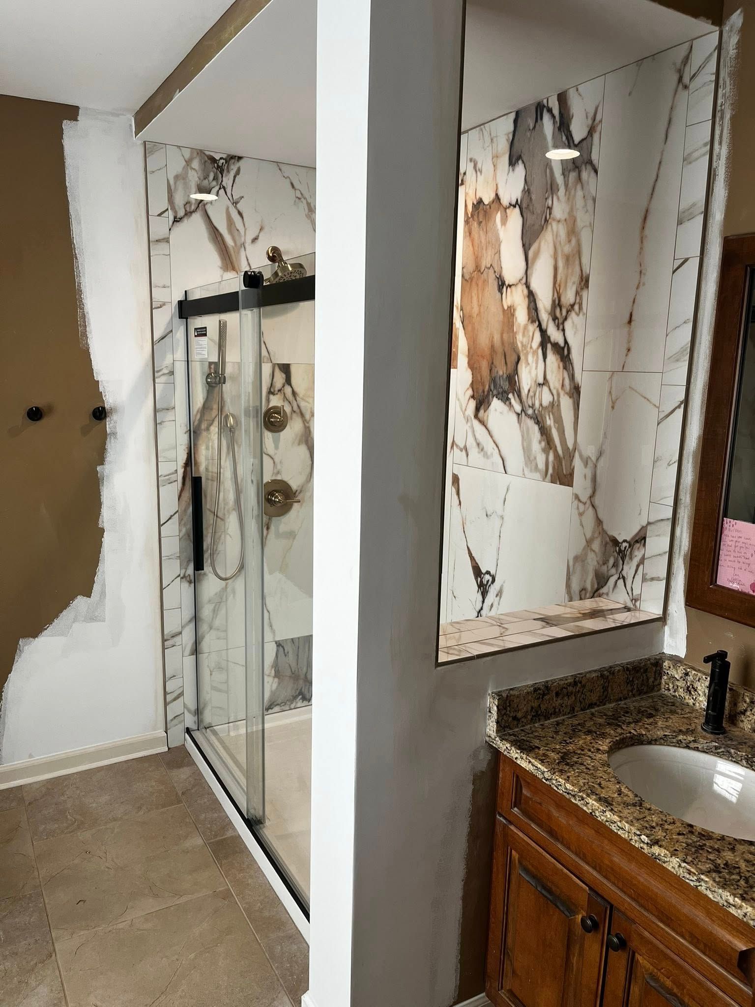 Bathroom renovation in progress, featuring a shower with marble-look tiles and vanity with granite countertop.