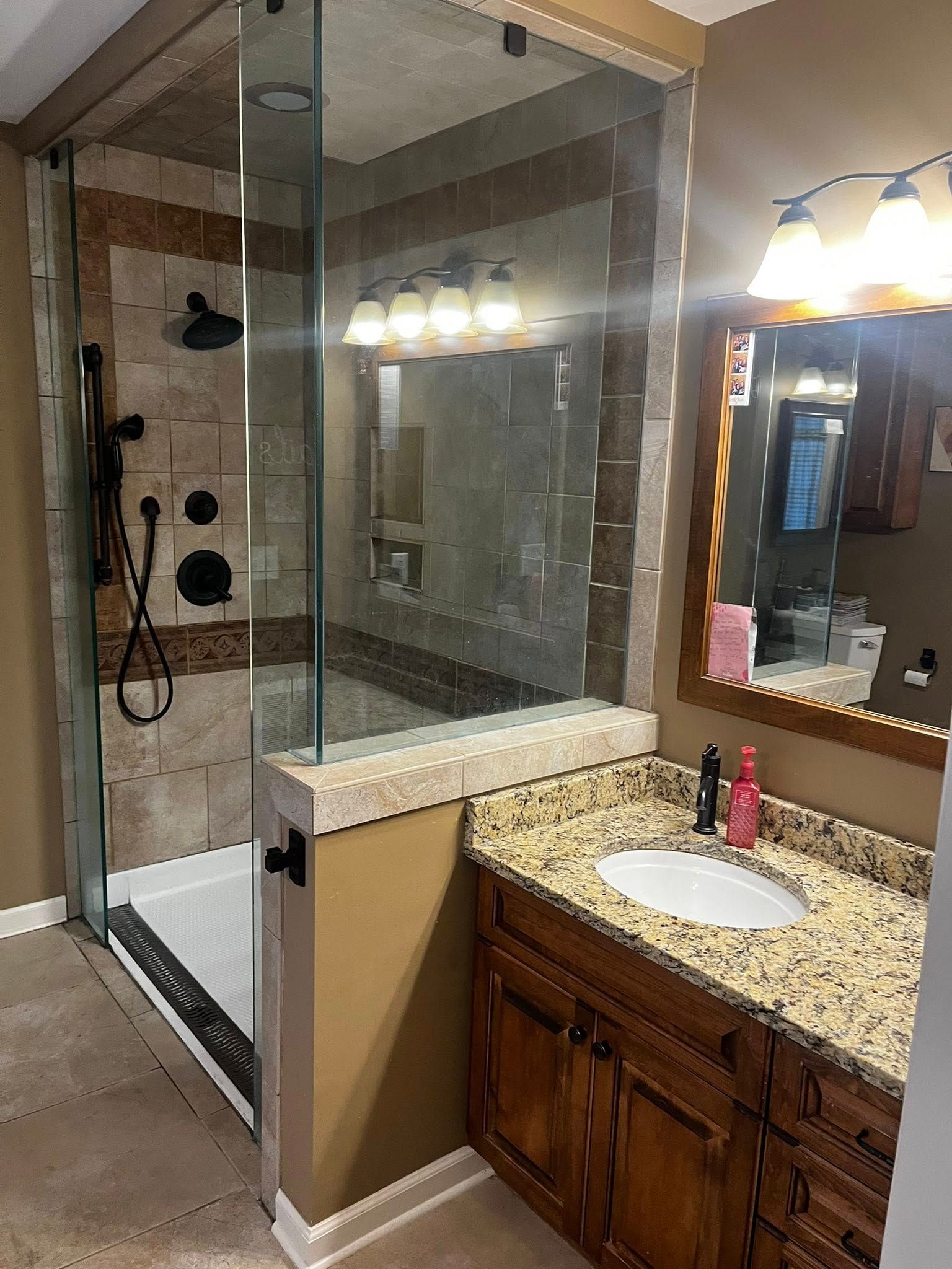 Bathroom with glass shower, granite countertop vanity, and brown cabinets.