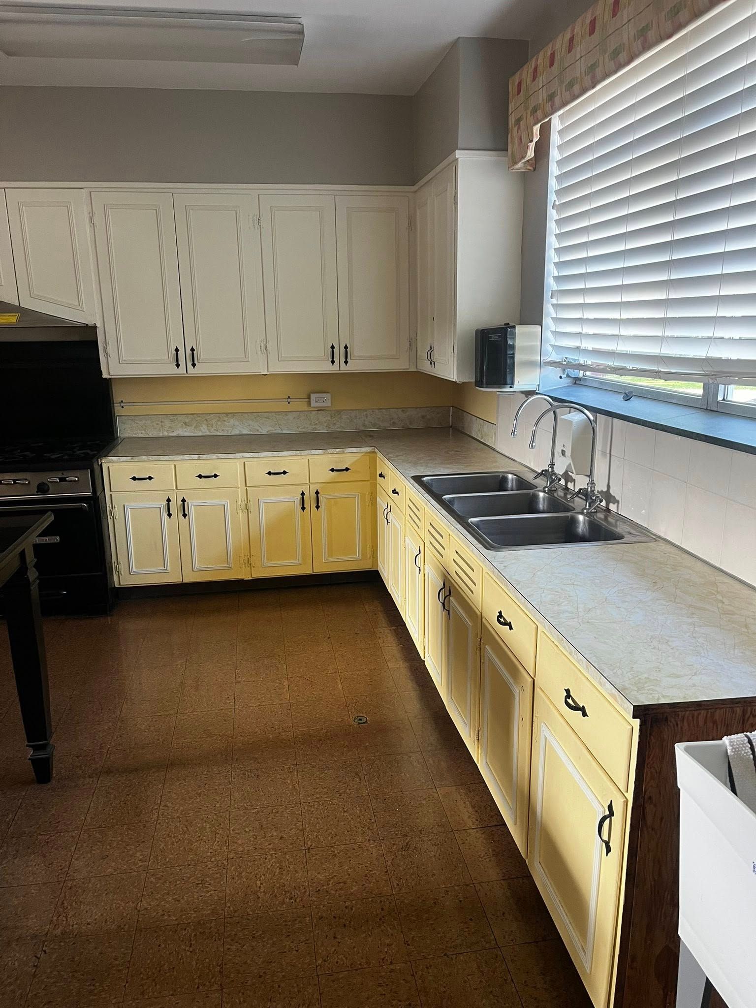 Yellow kitchen cabinets with light countertops and a sink by a window.