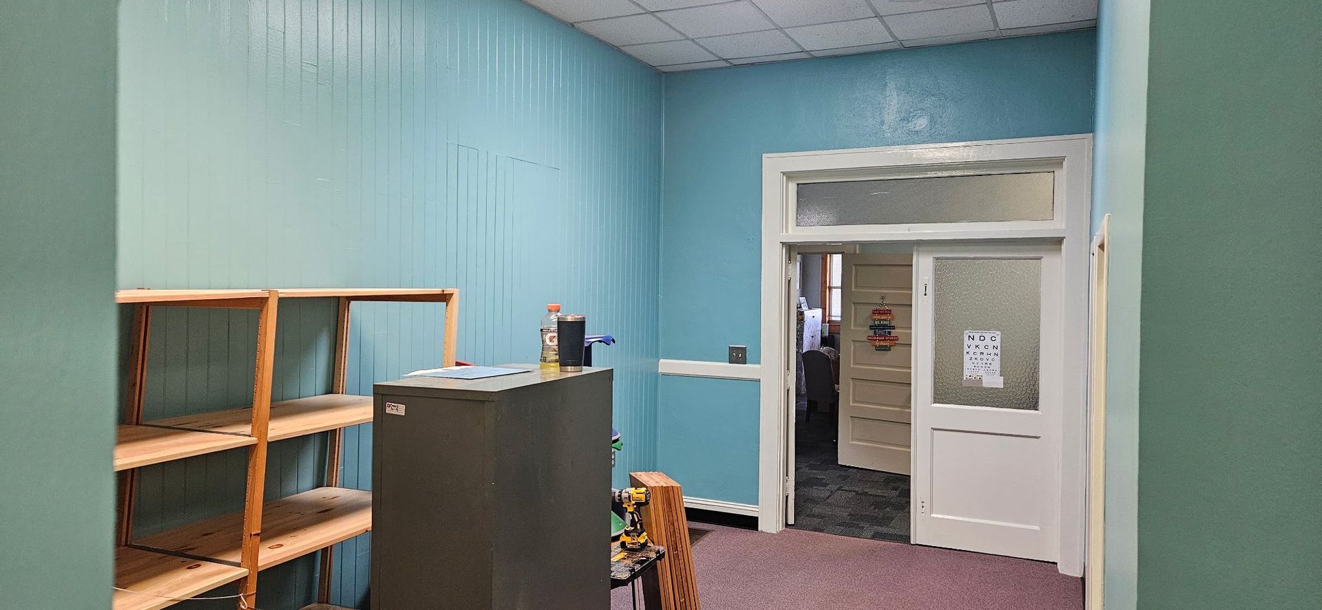 Interior room with blue walls, shelves, and a doorway leading to another room.