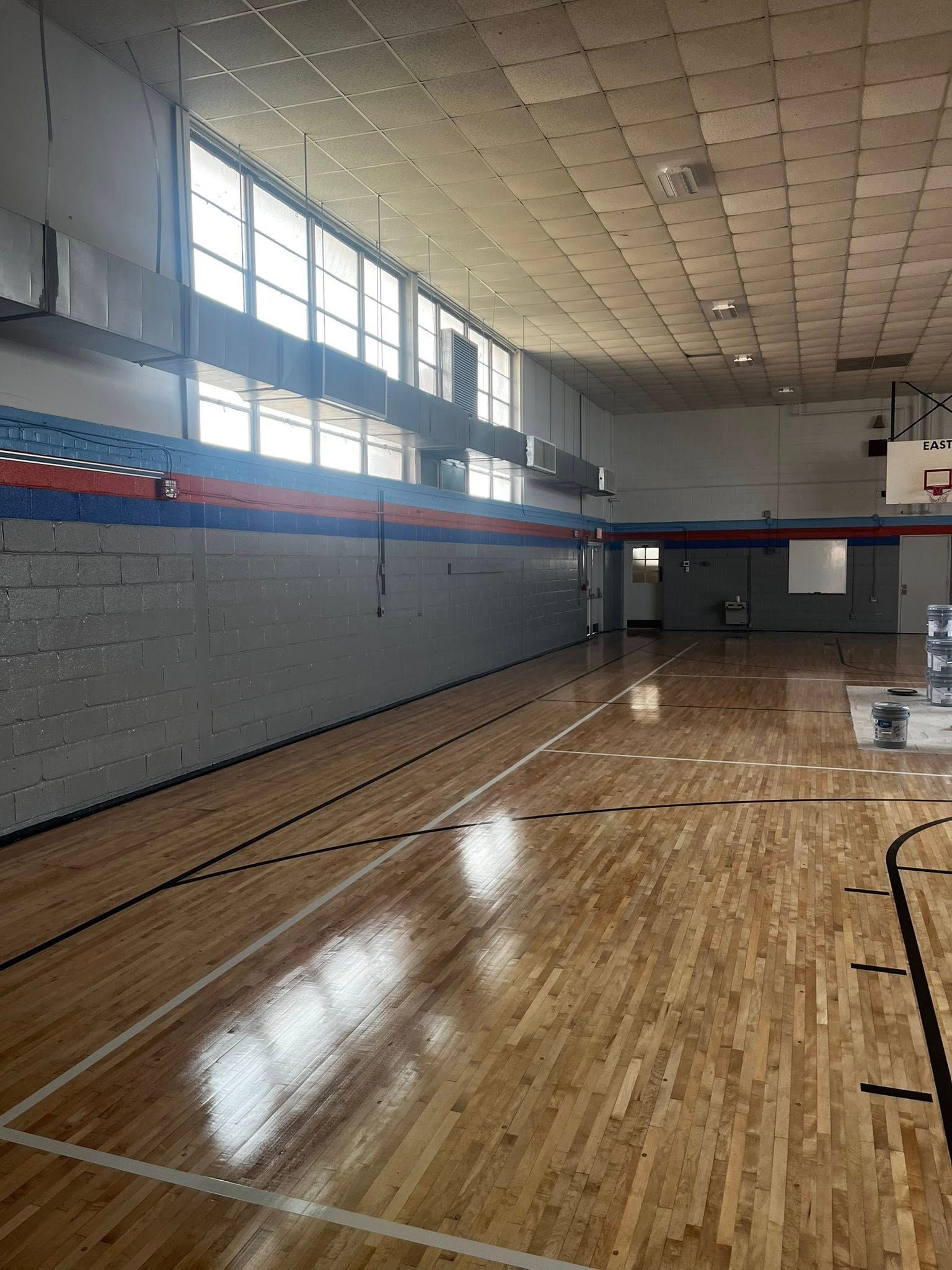 Empty gym with wood floor, high windows, and basketball hoops.
