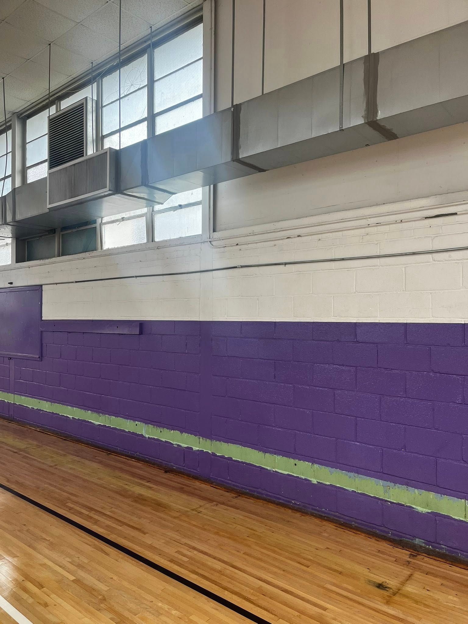 Gymnasium wall with purple lower section, green stripe, and white upper section. Air vents and windows.