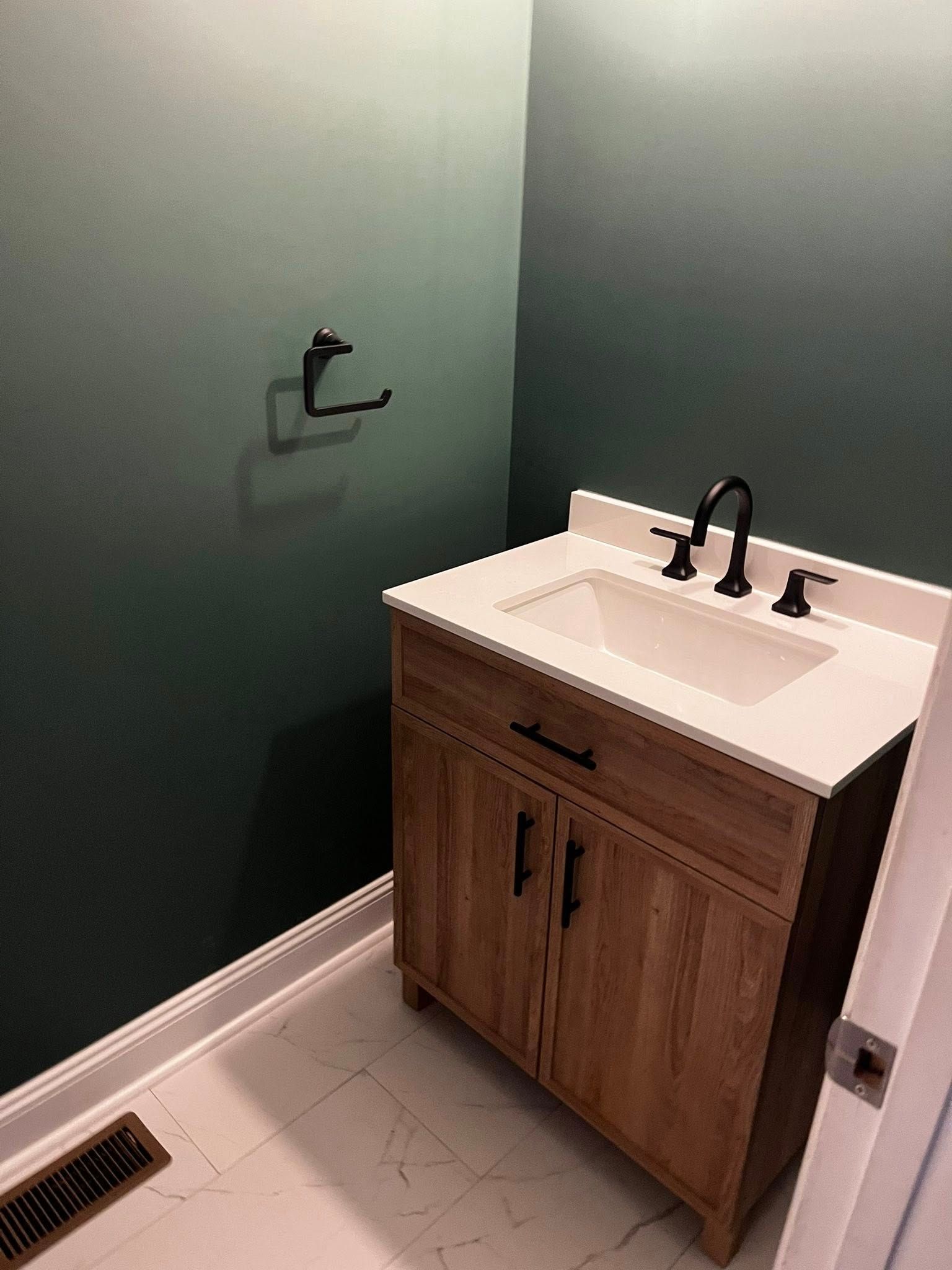 Bathroom with wooden vanity, white countertop, dark faucet, and green ombre wall.