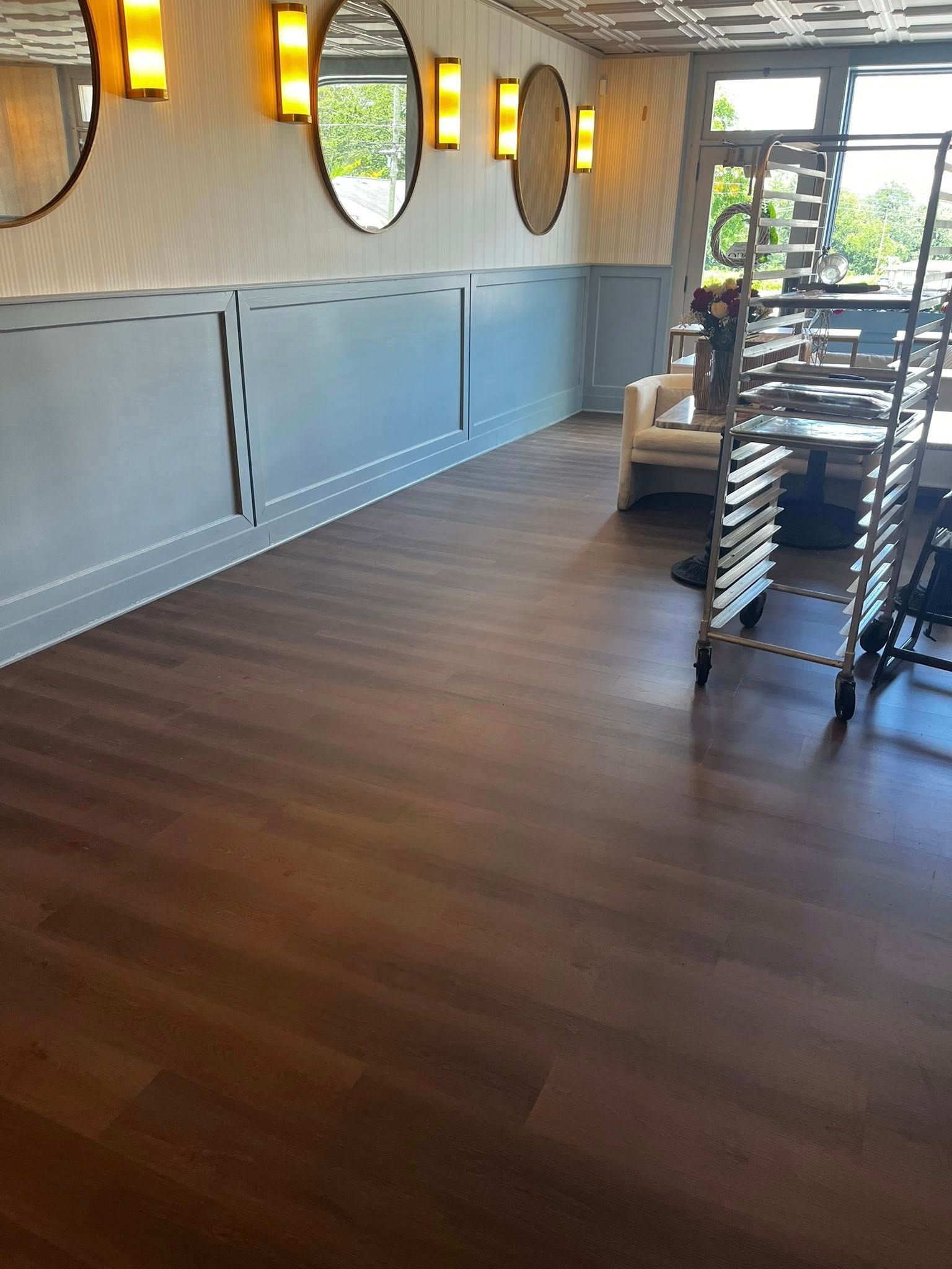 Interior view of a room with dark wood flooring, light blue paneling, and oval mirrors.
