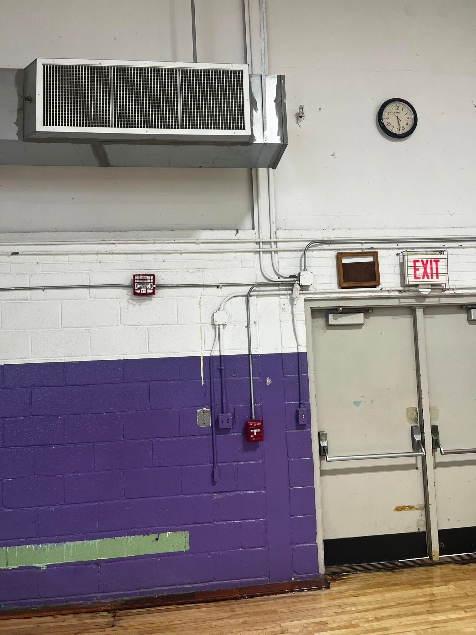 Purple and white painted brick wall with an air vent, clock, and exit doors.