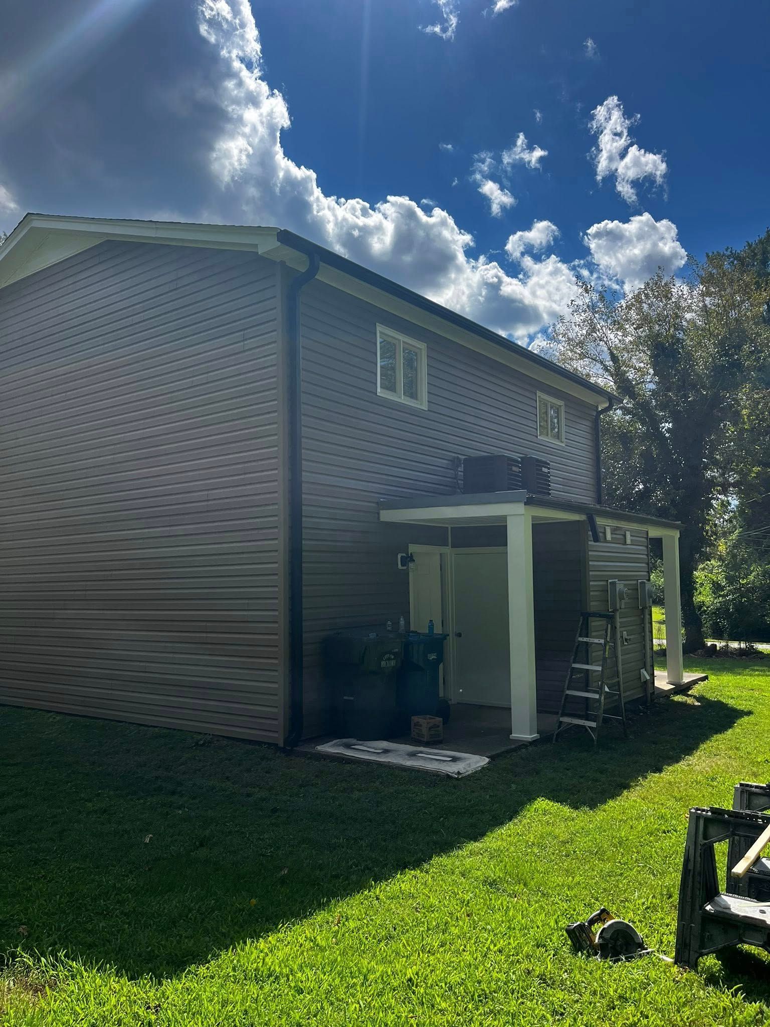 Two-story house with brown siding, white trim, and a porch under a bright blue sky.